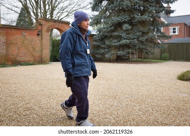 Elderly British Asian Woman Walking Outdoors In Winter. May Represent Senior Exercising Or Life At A UK Care Home Or Nursing Home.