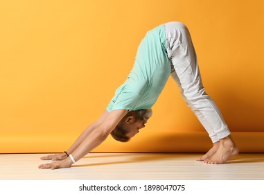 Elderly Brutal Male Yogi Practicing Yoga Concept, Standing In Exercise With Dog Face Down, Adho Mukha Shvanasana Pose, Training, In Light Casual Clothes, Full Length, Yellow Background