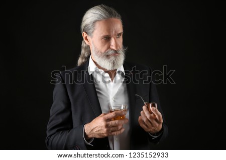 Elderly businessman with glass of whiskey and pipe on dark background