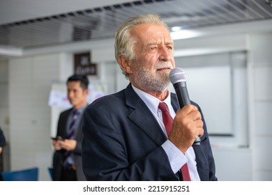 Elderly Businessman Holding A Microphone Speaking At A Meeting
