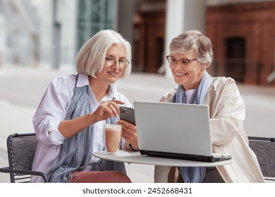 Elderly businesswomen at business meeting in outdoor cafe in the city. Beautiful mature senior women with gray hair discuss business matters with a laptop at the table. - Powered by Shutterstock