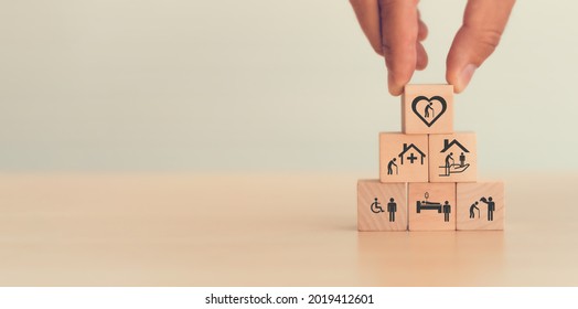 Elderly Care Concept. Hand Holds Wooden Cubes With Icons Related To Elderly Care, Medical, Rehabilitation Service, Nursing Care For Enhancing Quality Of Life In Elder People. Used Banner, Brochure.