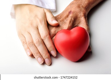 Elderly care concept, Young doctor holding senior patient hand to help and support with red heart, Family take care and nursing old people health, Healthcare insurance.
