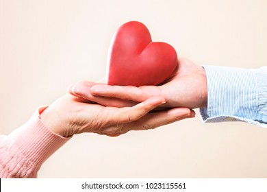 Elderly care concept. Young male doctor from health care facility passing a heart shape figure to senior woman. Close up of hands holding abstract love sign in nursing home. Background, copy space.