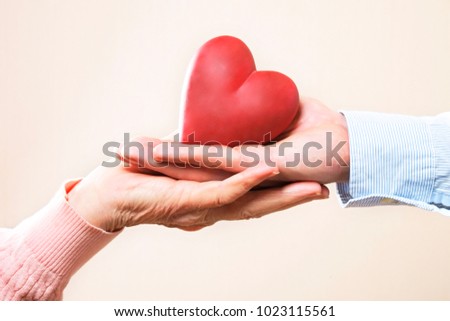 Elderly care concept. Young male doctor from health care facility passing a heart shape figure to senior woman. Close up of hands holding abstract love sign in nursing home. Background, copy space.
