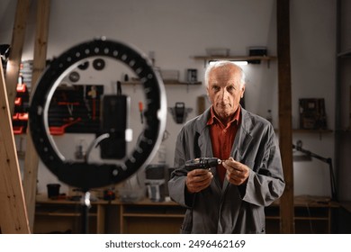 Elderly carpenter with drill recording vlog and communicating with his followers, livestreaming for his blog in social media in workshop. Blogging as business concept - Powered by Shutterstock