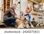 Elderly caucasian beautiful couple petting their dog together near their motorhome. Mature spouses husband and wife traveling by trailer with golden retriever