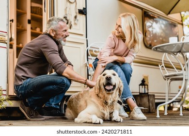 Elderly caucasian beautiful couple petting their dog together near their motorhome. Mature spouses husband and wife traveling by trailer with golden retriever - Powered by Shutterstock