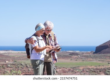 Elderly Caucasian Couple In Outdoors Activity On Hill Looking At Map. Landscape And Horizon Over Sea In Background