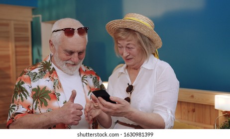 Elderly Caucasian man and gorgeous woman looking at screen of smartphone. Happy old couple reviewing photos, laughing. Like, thumbs up. Inside. - Powered by Shutterstock