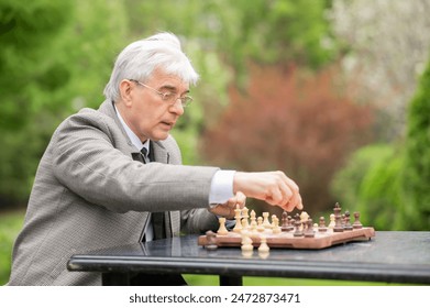 Elderly Caucasian man playing chess outdoors.  - Powered by Shutterstock