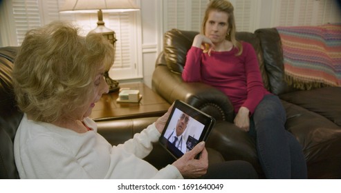 An elderly Caucasian woman and her daughter engaged in a video conference with her doctor via a telehealth or telemed app on a wireless mobile device tablet pc.