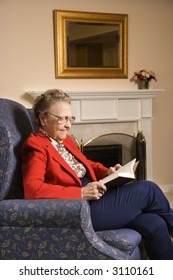 Elderly Caucasian Woman Reading Book In Chair At Retirement Community Center.