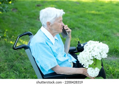 Elderly Caucasian Woman Using Mobile Phone On Wheelchair At The Garden