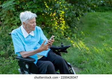 Elderly Caucasian Woman Using Mobile Phone On Wheelchair At The Garden