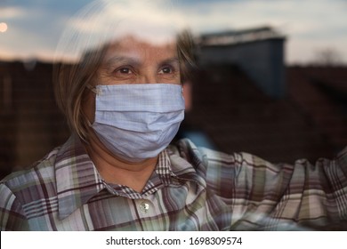 Elderly Caucasian Woman Wearing Handmade Protective Face Mask,nursing Care Home,looking Outside The Window With Sadness In Her Eyes,self Isolation Due To The Global COVID-19 Coronavirus Pandemic,hope