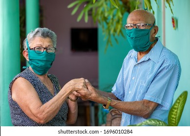 An elderly couple, both wearing face mask and glasses and holding hands