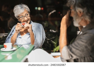 Elderly couple enjoying coffee at an outdoor café, with the man taking a photo of the woman. - Powered by Shutterstock