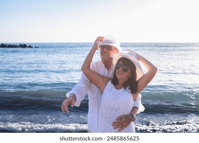 Elderly couple enjoying a sunny day at the beach, smiling and embracing each other while dressed in light summer clothes, conveying love, happiness, and companionship - Powered by Shutterstock