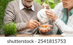 Elderly couple enjoying tea outdoors. Senior man and woman pouring tea. Happy elderly couple sharing tea time. Outdoor tea with senior couple. 