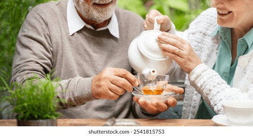 Elderly couple enjoying tea outdoors. Senior man and woman pouring tea. Happy elderly couple sharing tea time. Outdoor tea with senior couple.  - Powered by Shutterstock