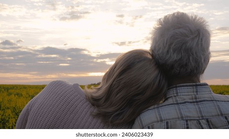 Elderly couple enjoys beautiful sunset view. Married couple standing in blooming rural field outdoor. Woman lovingly puts head on husbands caring shoulder. Supporting people in old age and taking care - Powered by Shutterstock