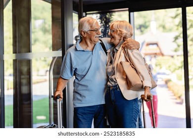 An elderly couple enters a hotel lobby, pulling their suitcases. They are dressed casually, smiling, and ready for travel, suggesting they are on a vacation or trip. - Powered by Shutterstock