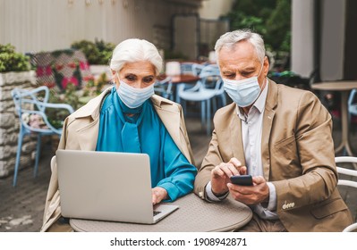 Elderly Couple With Face Masks Looking At Computer Laptop - People During Coronavirus Pandemic Quarantine, Video Call Online With Family To Respect Social Distancing