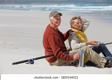 Elderly couple with a fishing rod sitting on a sunny beach and enjoying coffee. - Powered by Shutterstock