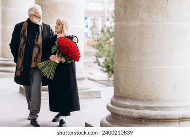 Elderly couple, handsome old man gives a huge bouquet of red flowers to his lady on a valentines day - Powered by Shutterstock