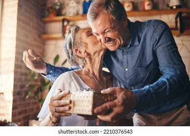 Elderly, couple and happy with gift, surprise and kiss on face together in home. Man, woman and retirement show love, romance and happiness giving present for anniversary, birthday or mothers day - Powered by Shutterstock