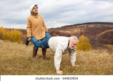 Elderly couple having fun and playing the wheelbarrow in nature.  "Woman carried his husband until old age."