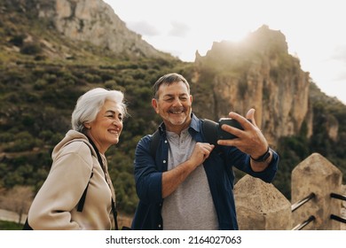 Elderly couple having a video call while standing on a hilltop. Happy senior couple enjoying a recreational hike outdoors. Adventurous couple having a good time together after retirement. - Powered by Shutterstock