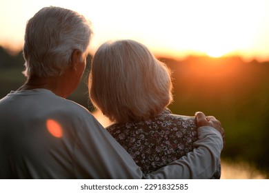 Elderly couple hugs and looks at the sunset. Rear view - Powered by Shutterstock