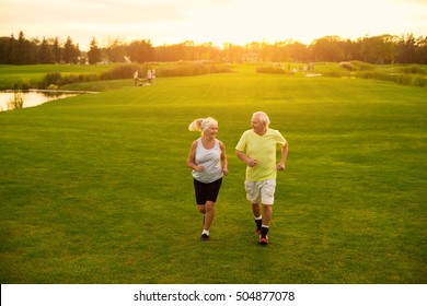 Elderly Couple Is Jogging. Smiling People On Meadow. Be In Motion. The Lightness Of Moves.