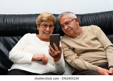 Elderly couple looking at the mobile phone sitting on the sofa at home