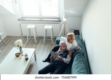 Elderly couple lying on the sofa holding a digital tablet - Powered by Shutterstock