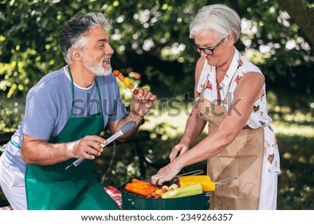 Elderly couple are making barbeque, vegetables, and drinking beverages while enjoying and making memories.