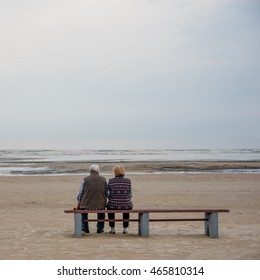 Elderly couple on the beach sitting on the bench.