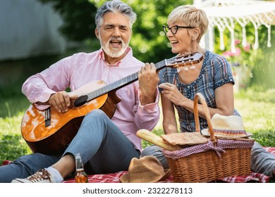 Elderly couple playing guitar and singing while sitting on the grass. They are having a picnic and are making memories - Powered by Shutterstock