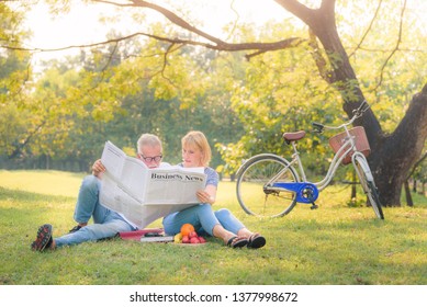 Elderly Couple Reading Newspaper In Garden At Sunset. Concept Couple Elder Love.