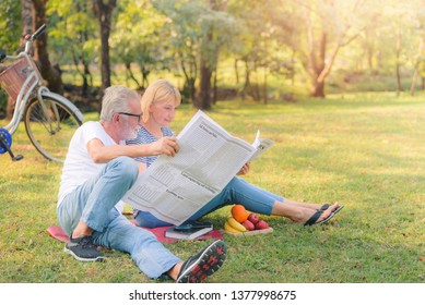 Elderly Couple Reading Newspaper In Garden At Sunset. Concept Couple Elder Love.