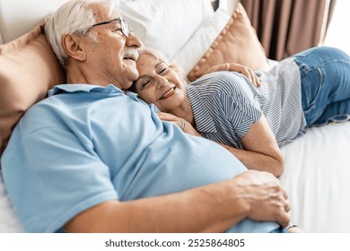 An elderly couple relaxes together on a hotel bed, smiling and enjoying a peaceful moment - Powered by Shutterstock