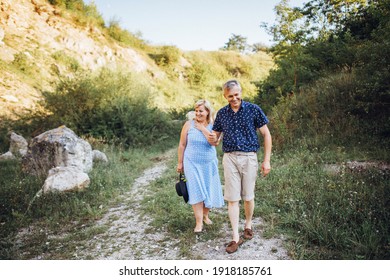 Elderly Couple Resting In Nature With Rocks In Summer Time. Walking Together By Grass