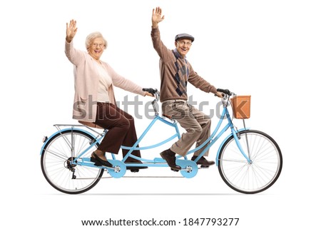 Elderly couple riding a blue tandem bicycle and waving isolated on white background