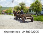 An elderly couple riding in a horse-drawn cart along the road in the Romanian village of Viscri