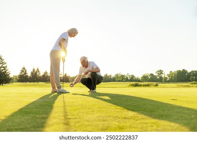 elderly couple seniors playing golf on golf course at sunset, old man and woman practicing with golf clubs in nature, husband and wife in white uniform actively relaxing - Powered by Shutterstock