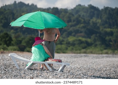 An elderly couple sets up a sun umbrella on the beach. - Powered by Shutterstock