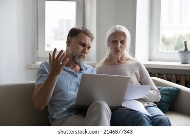 Elderly Couple Sit On Sofa At Home With Laptop Sorting Out Papers, Reviewing Expenses, Feel Angry Due To Utility Bills Going Up. Financial Crisis, Bank Debt Notice, Bankruptcy, Lack Of Money Concept