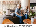 An elderly couple sits together in a modern hotel lobby, engaged in conversation. Their luggage is nearby, suggesting they are either waiting or checking in for their trip.